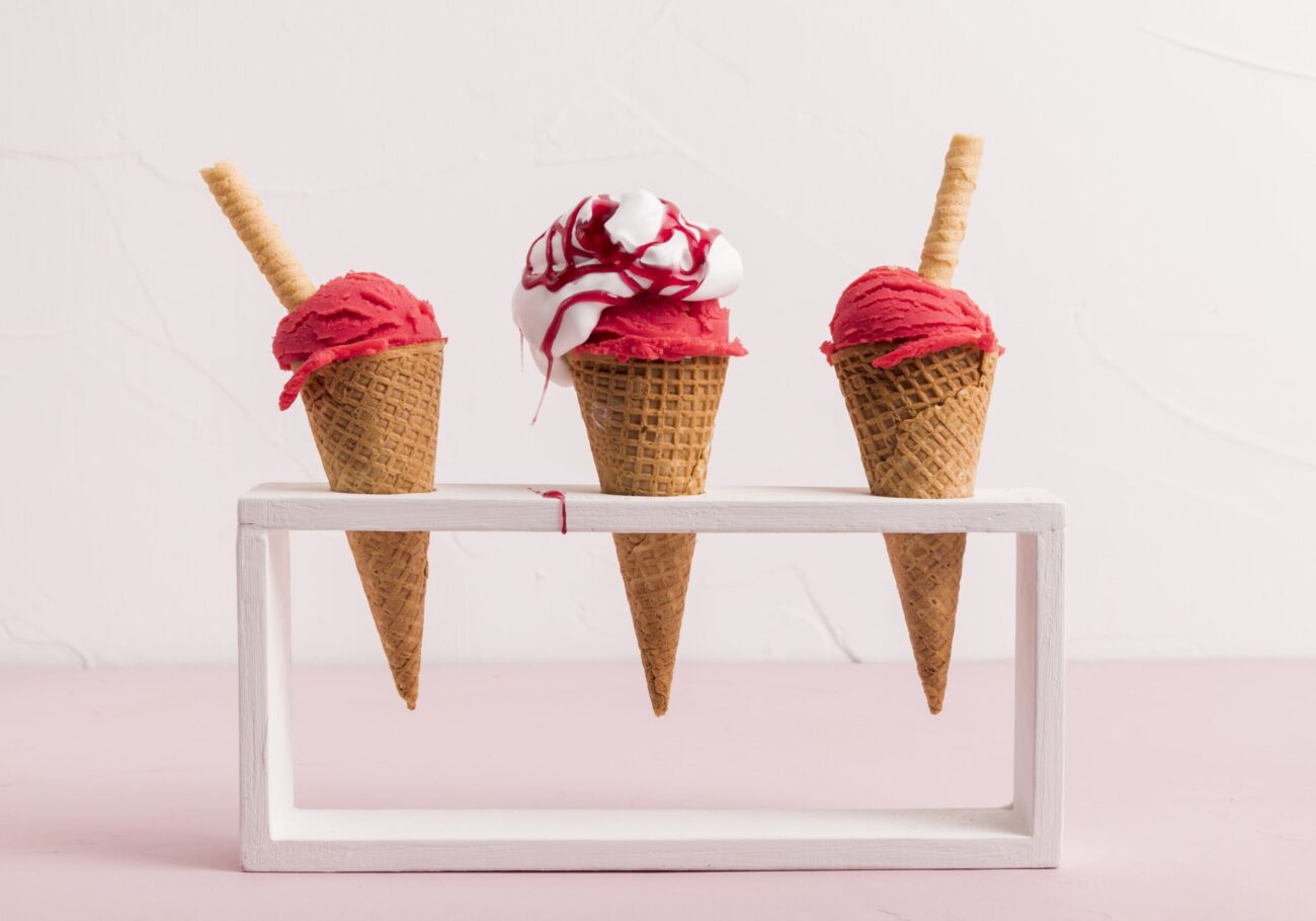 red-ice-cream-scoop-in-cones-with-syrup-and-waffle-straw-on-stand-min